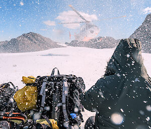 Expeditioners shelter from snow blowing from the rotors of a helicopter