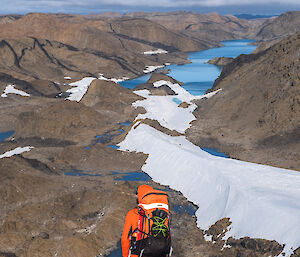 An expeditioner wearing an orange backpack surveys a snowy and rocky landscape