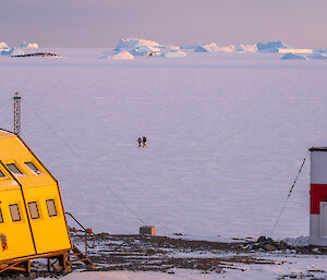 A view between two Antarctic buildings across onto the sea ice, with icebergs visible in the distance
