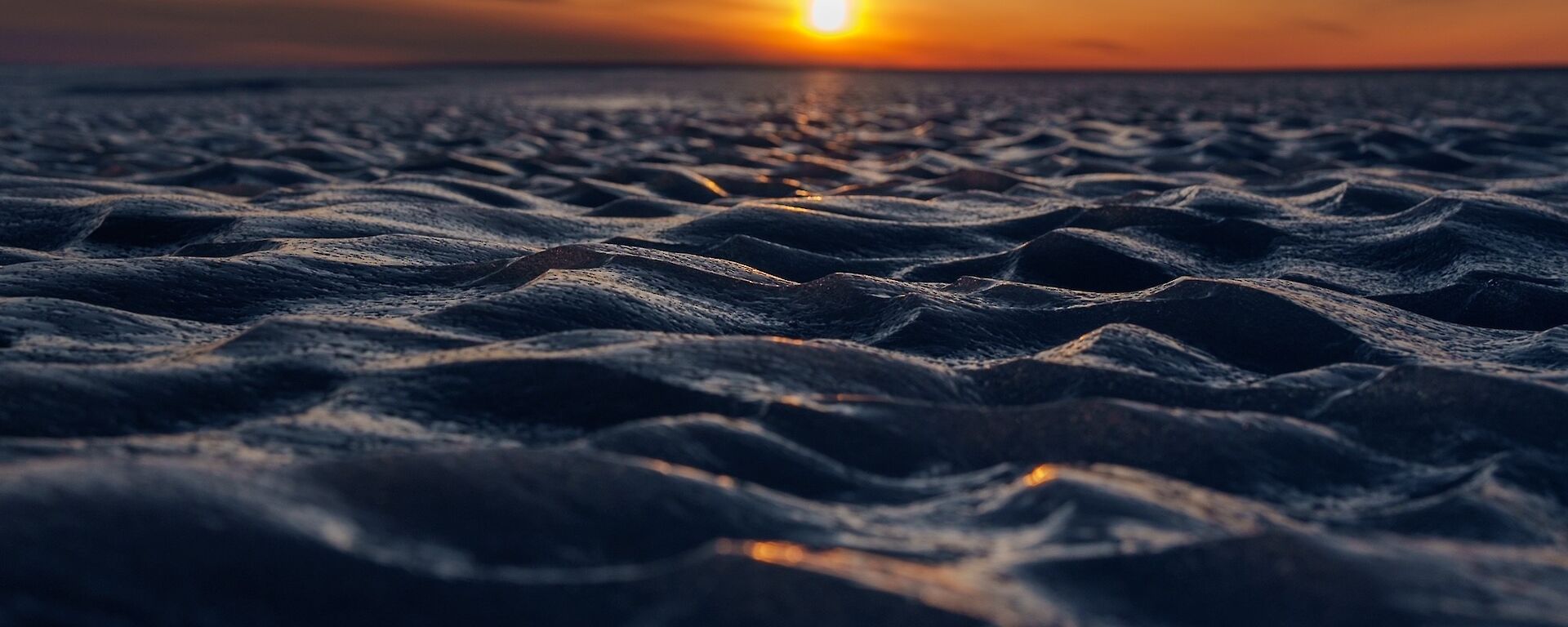 A ground-level photo of icy patterns across the plateau, with sun low in the horizon in the background