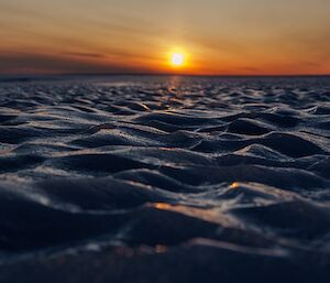 A ground-level photo of icy patterns across the plateau, with sun low in the horizon in the background
