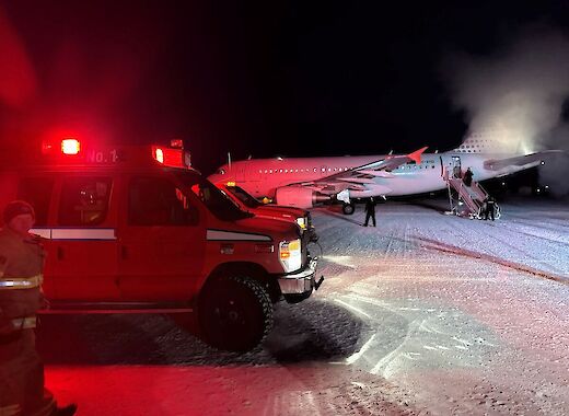 A large place and emergency vehicle are parked on the ice in the dark.
