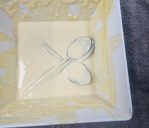 A bowl almost empty with custard and three spoons at the bottom