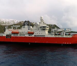 A large white and red ship with snow-covered mountains behind it