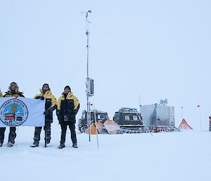 four expeditioners on the ice holding a flag