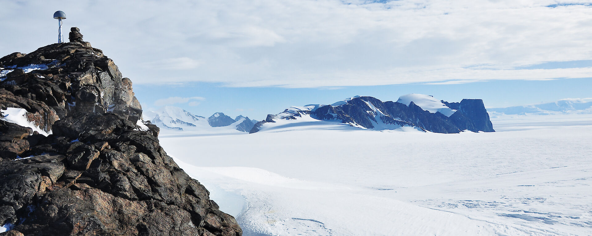 A white icy landscape with brown rocks in the foreground, under clouds and blue sky
