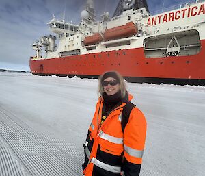 A woman in hi vis stands on ice with a big red and white ship in the background
