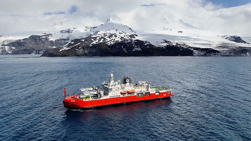 Red and white ship on still water with a snow covered volcano behind it