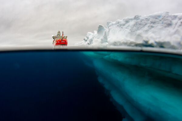 Underwater view of a ship sitting in the ocean next to an ice shelf