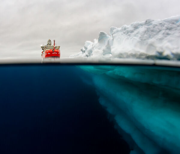Underwater view of a ship sitting in the ocean next to an ice shelf