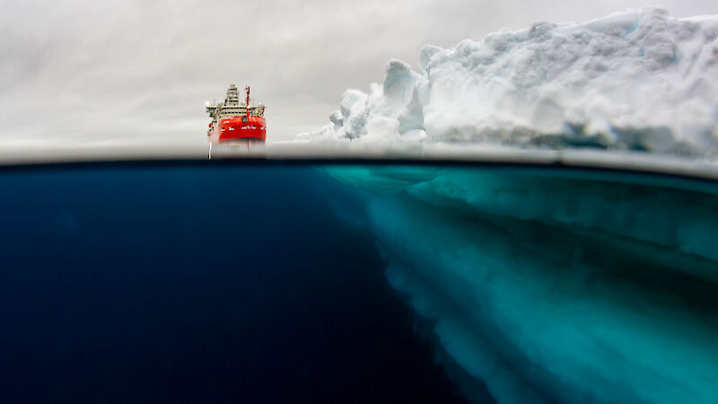 Underwater view of a ship sitting in the ocean next to an ice shelf