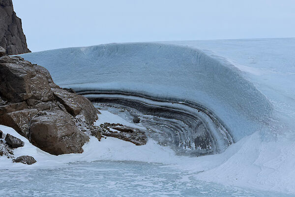 A build-up of ice that has created a layered wall around a large rock feature