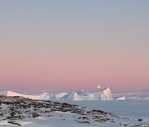 photo taken standing on a rocky outcrop covered in snow, with sea ice, ice bergs and a moonlit clear sky in background