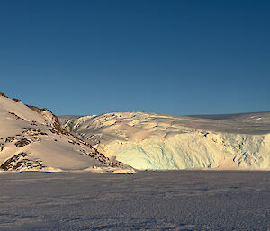 photo taken on the sea ice with ice cliff alongside a snow-covered rocky outcrop