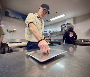 An expeditioner prepares to spin the Bain-marie lid on a kitchen top bench