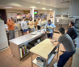 Expeditioners standing around a kitchen steel bench waiting for lid-spinning to start