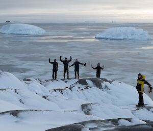 A group of expeditioners stand on top of ice covered boulders with the ocean in the background.