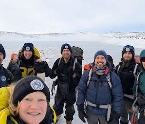 A group of 7 expeditioners wearing warm clothing and backpacks stand on snow and ice