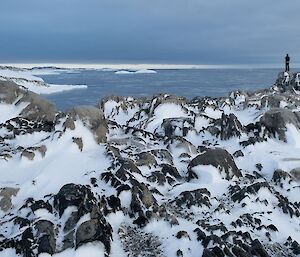 a person stands amid rocky and snowy peaks that tower above the surrounding ocean.