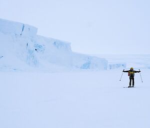 a person on skis stands on white snow, beside white cliffs, underneath a white sky.