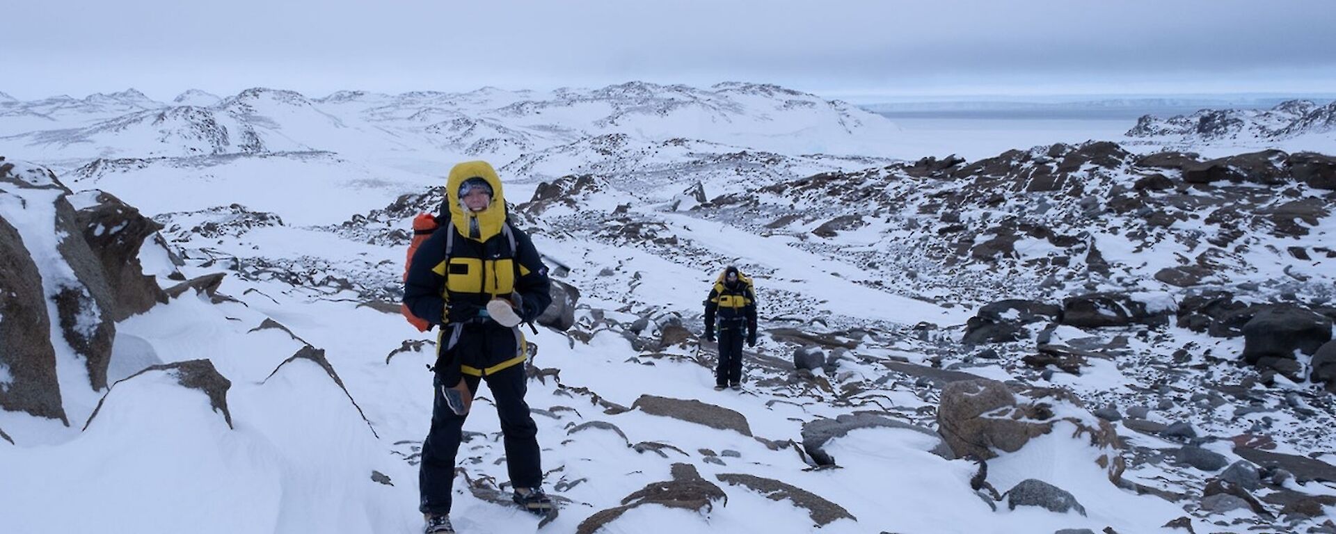 Expeditioner wearing black and yellow standing in a rocky and icy landscape