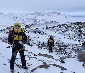 Expeditioner wearing black and yellow standing in a rocky and icy landscape
