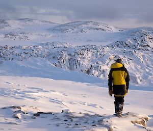 Expeditioner wearing black and yellow walking through rocky and snowy terrain.