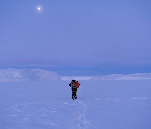 an expeditioner treks through a snowy landscape with a single star shining above the horizon.