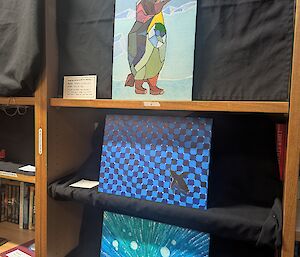 Three pictures featuring penguins and ice are displayed on shelving