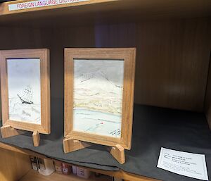 Two pictures in wooden frames sit on small easels