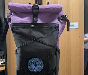 A purple and black backpack hangs on a coat rack
