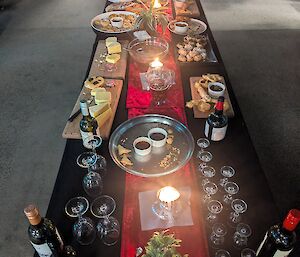 A table covered with a black tablecloth and a red runner displays food and beverages