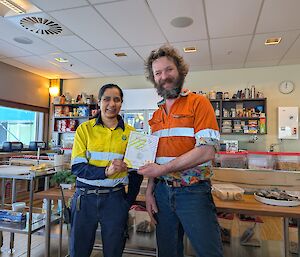 An expeditioner in yellow high visibility clothing presents a certificate to another expeditioner in an orange high visibility jumper
