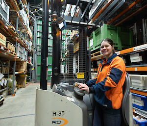 A woman in orange hi vis driving a fork lift in a warehouse