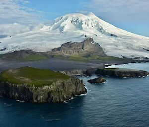 A snow covered mountain rising from the sea