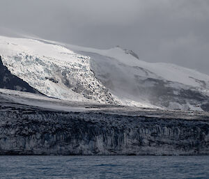 A glacier covered in black volcanic dust, coming down to the coast.