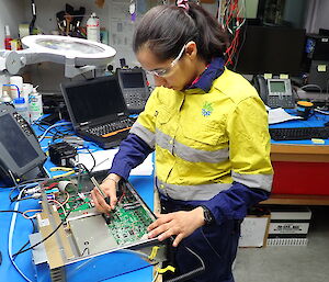 A woman in yellow work wear, working on electronics in a workshop