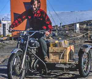 a historic picture of an expeditioner riding a motorcycle customised with an extra rear wheel/sidecar platform