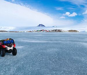 a lone quad bike on the sea ice, with Mawson Station in the far background