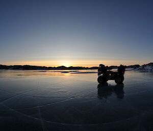 a quad bike in shadows on the ice, as the sun sets below the horizon