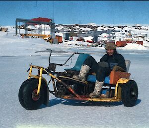 a historic picture of an expeditioner riding what appears to be an old 'home-made' tricycle motorbike out the front of Mawson Station