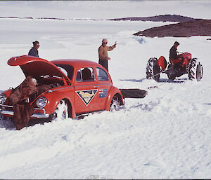 historic picture of a red ANARE Volkswagen Beetle car stuck in the snow, being recovered by a tractor
