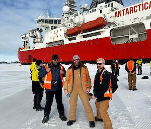 Three people in high visibility vests pose on the sea ice infront of a large red ship