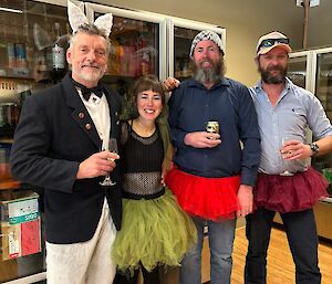 A group of four people, a man dressed as an elegant rabbit/fox, a woman in a green tutu and two men in red tutus, posing at a party