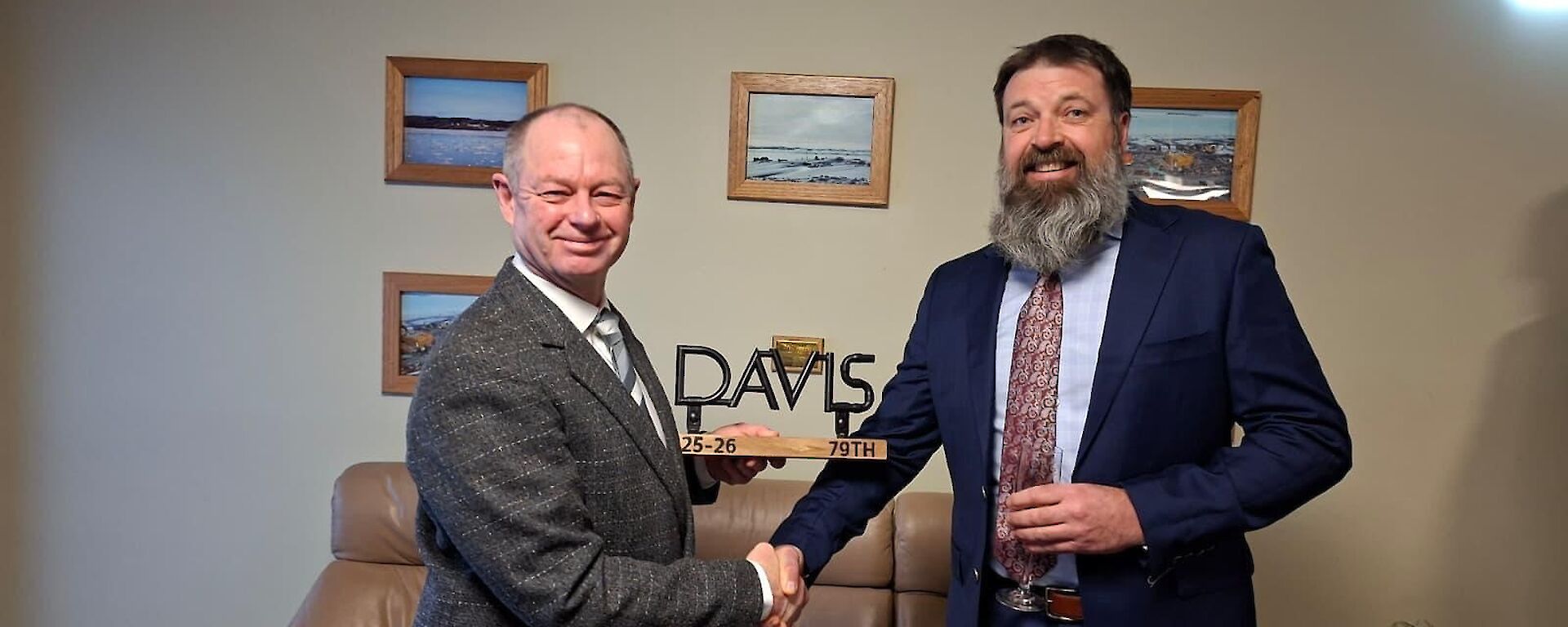 Two men in suits as one is presented with a sculture of the word 'Davis' mounted on a wooden base