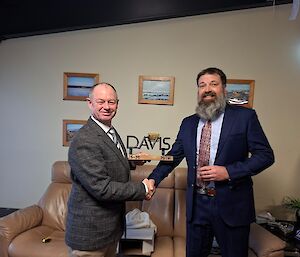 Two men in suits as one is presented with a sculture of the word 'Davis' mounted on a wooden base