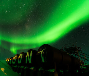 Mawson's fuel farm sign lit up with overhead green aurora trails