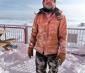 An expeditioner covered in snow and ice after digging a clearing on the porch.