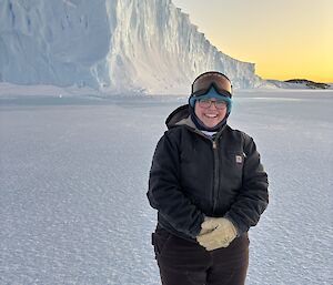 A smiling expo standing on the sea ice, in front of a large ice cliff