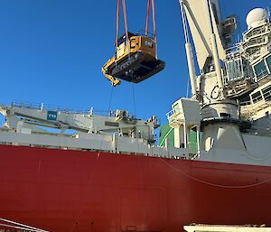A crane lifts a small yellow digger onto a big red ship